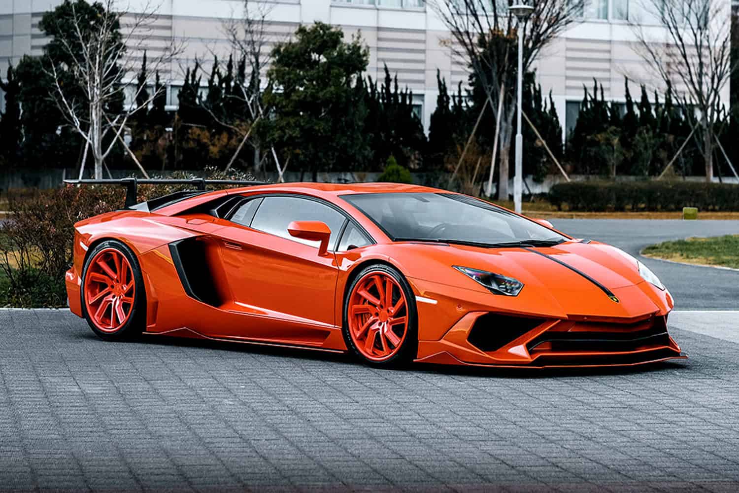 Orange Lamborghini Aventador with custom Lexani wheels in an urban setting.