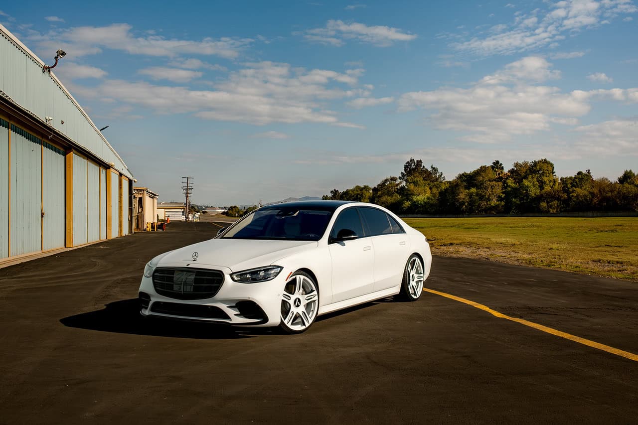 Elegant white luxury sedan parked on an open asphalt area with a clear sky.