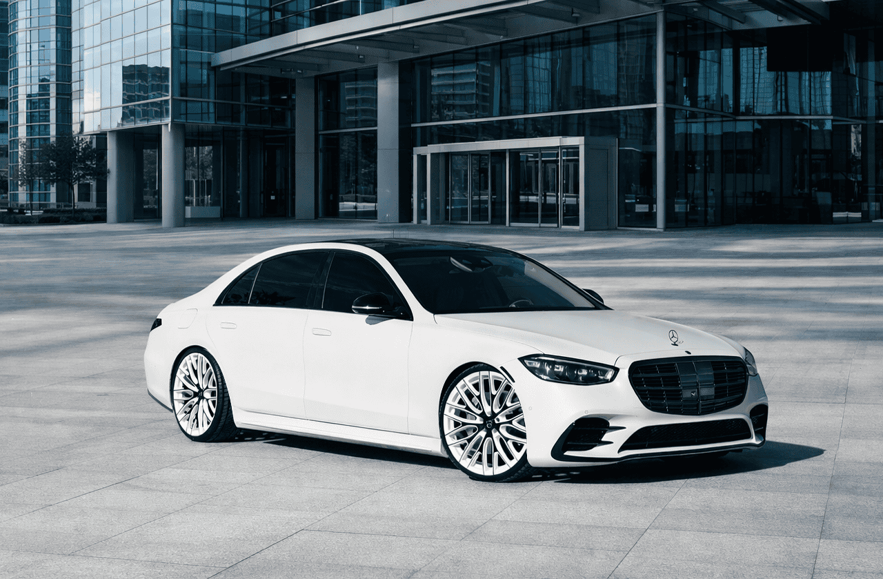 Sleek white Mercedes-Benz luxury sedan featuring custom Lexani wheels, parked in front of a contemporary office building.